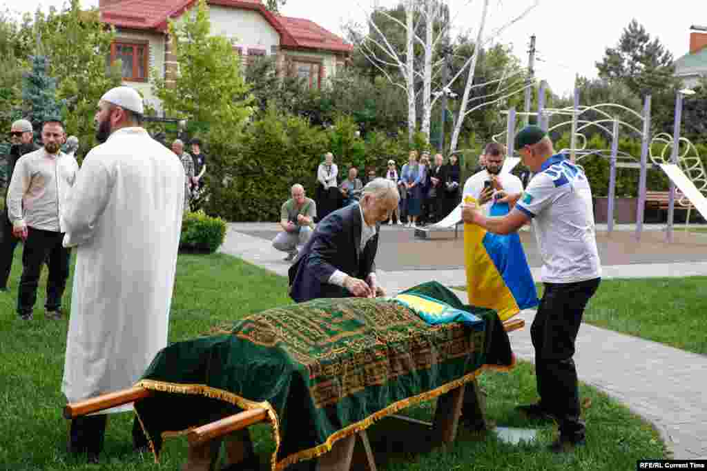 Церемония прощания с Айдосом Садыковым прошла в селе Чайки под Киевом. Организацию похорон взяла на себя крымскотатарская община, с представителями которой дружил покойный.&nbsp; На фото: лидер крымских татар Мустафа Джемилев (в центре) укрывает тело Айдоса Садыкова флагом Казахстана. Киевская область, 5 июля 2024 года&nbsp;