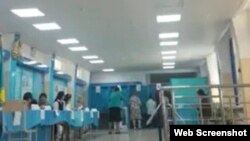 Женщина в бирюзовом жакете и черной юбке, присутствующая в качестве члена комиссии, опускает в урну для голосования бюллетени