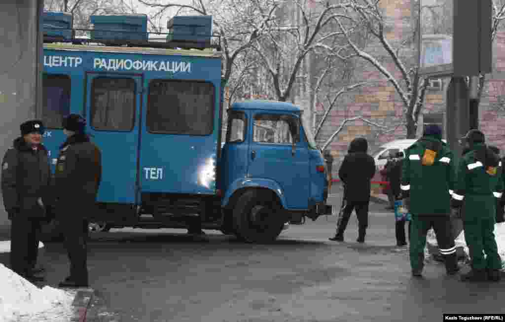 Полицейские рядом с машиной, в которой расположился центр радиофикации, стоят позади площади, где проходил митинг в честь 25-летия Декабрьских событий. Алматы, 17 декабря 2011 года.