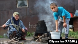 Жена и сын Зулкайнара Ергашева кипятят воду для чая на огне на улице, экономя газ. Семья переехала с юга на север Казахстана два месяца назад. Село Покровка, 21 июля 2016 года.