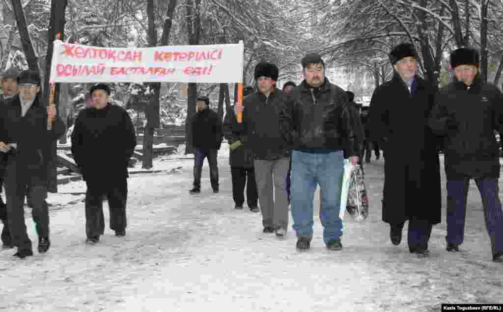 Политик Хасен Кожа-Ахмет и его сторонники идут к офису президентской партии &quot;Нур Отан&quot;, чтобы выразить протест действиям властям в Жанаозене во время массовых беспорядков. 